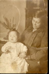 Sepia-toned portrait of an African American mother seated with her infant child on her lap. The mother looks down gently at the baby while the child faces the camera in a soft studio setting.